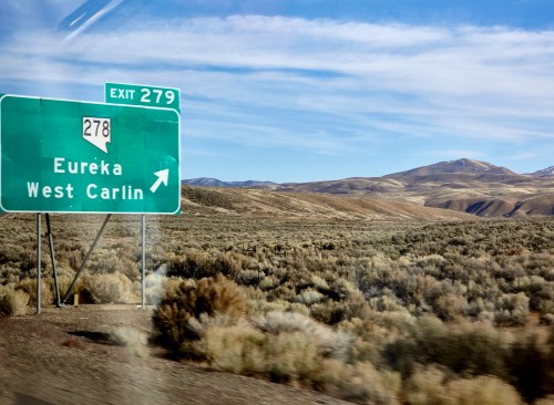 Green highway sign indicating Exit 278 for Eureka and West Carlin, with a desert landscape in the background.