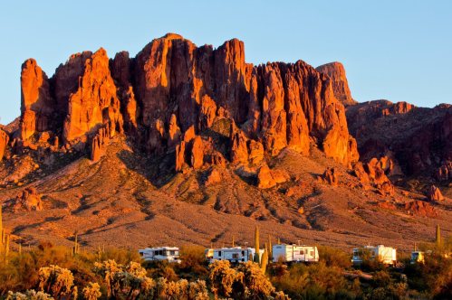 Orange rocks appear ablaze in the sun at Lost Dutchman State Park in Arizona, with several RVs in the foreground