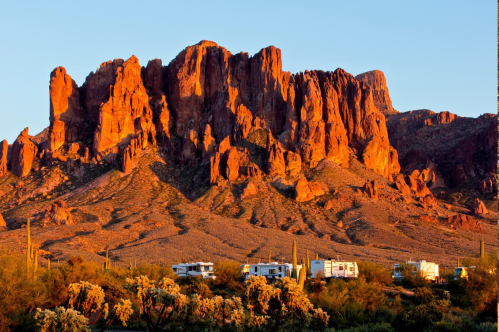 Orange rocks appear ablaze in the sun at Lost Dutchman State Park in Arizona, with several RVs in the foreground
