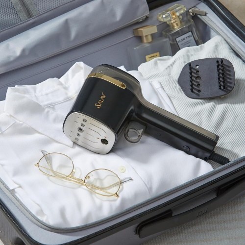 A suitcase packed with a black hair dryer, a white shirt, glasses, and a bottle of perfume.