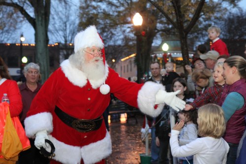 Santa Claus greets children and families at a festive outdoor event, surrounded by holiday decorations and lights.