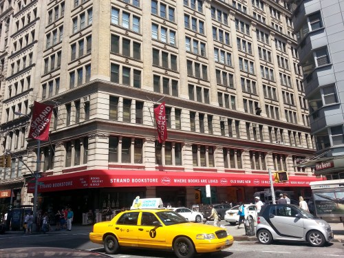 Exterior of the Strand Bookstore with red awnings, surrounded by pedestrians and yellow taxis on a sunny day.