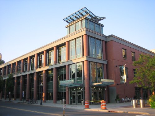 Modern brick building with large windows and a glass roof, featuring a welcoming entrance and surrounding greenery.