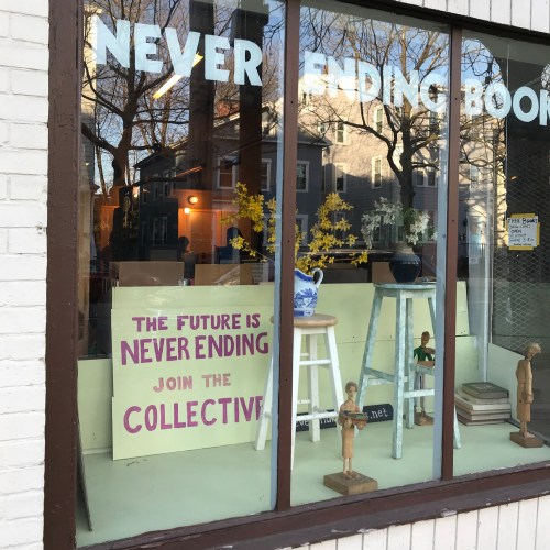 A storefront window displays a sign reading "The future is never ending, join the collective," with decorative items inside.