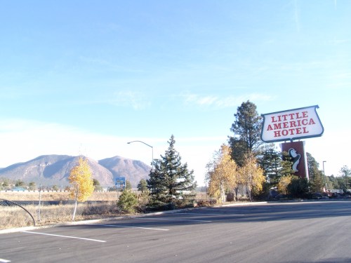 Sign for Little America Hotel with mountains in the background and trees in autumn colors. Clear blue sky above.