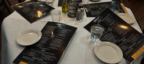 A table set with white plates, glasses of water, and menus at a restaurant.
