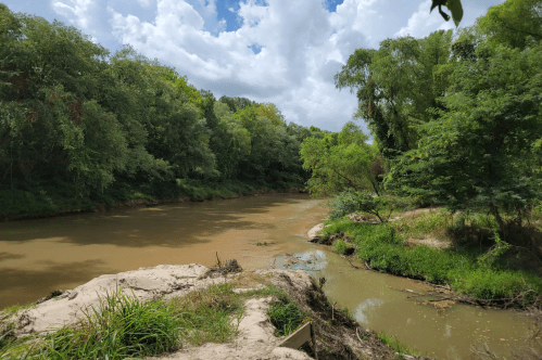 A serene river flows through a lush green landscape under a partly cloudy sky.