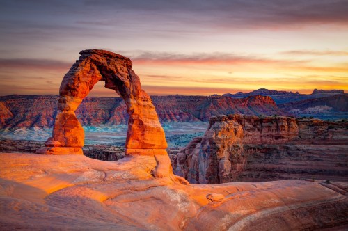 A stunning sunset view of Delicate Arch in Arches National Park, with vibrant colors illuminating the rock formations.