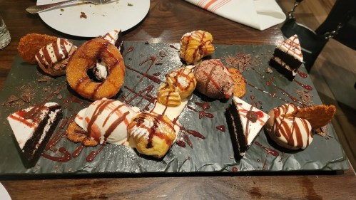 A dessert platter featuring various pastries, cakes, and ice cream drizzled with chocolate and strawberry sauce.