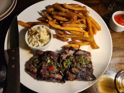 A plate with grilled steak topped with green sauce, served with fries and a side of coleslaw.