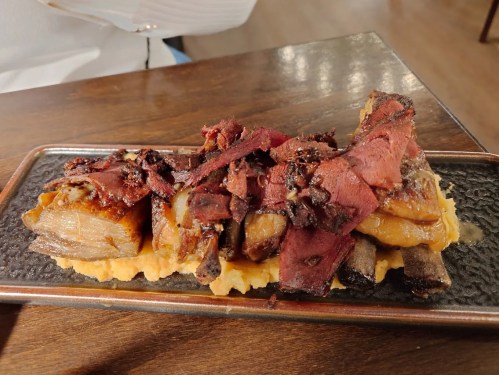 A plate of succulent meat ribs topped with crispy bits, served on a textured black dish.