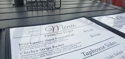 Menu on a table featuring items like hand-battered cod and chicken strips, with prices listed.