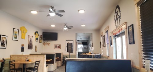 Interior of a casual restaurant with wooden booths, ceiling fans, and wall decor including framed posters and a TV.