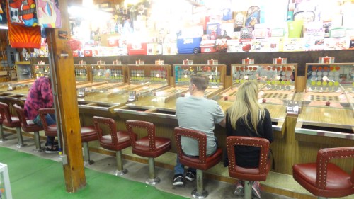 A vintage arcade with three players at slot machines, surrounded by colorful game displays and retro decor.