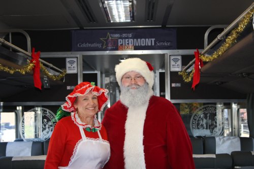 A man in a Santa suit and a woman in a holiday dress smile inside a decorated bus.
