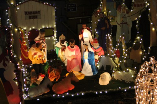 Nativity scene with illuminated figures of Mary, Joseph, and animals, surrounded by festive lights.