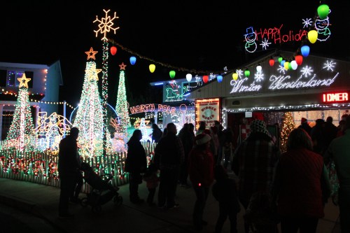 A festive display of colorful holiday lights and decorations, with people enjoying the scene at night.