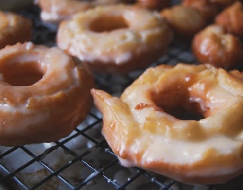 Glazed donuts cooling on a wire rack, showcasing a golden-brown color and shiny icing.
