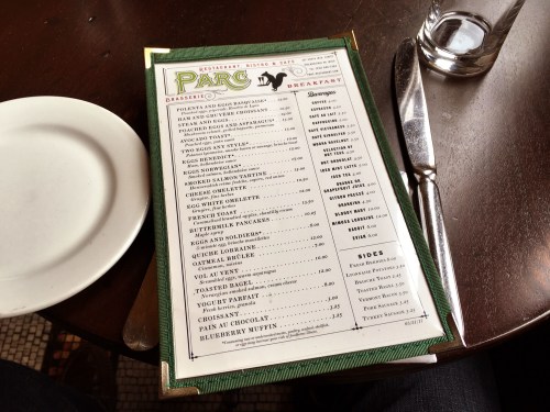 A breakfast menu from Parc restaurant, featuring various egg dishes, sides, and beverages, on a wooden table.