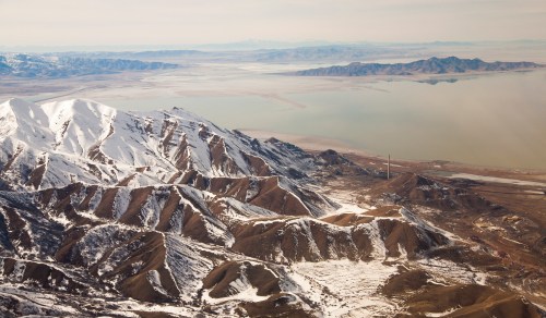 Aerial view of snow-capped mountains overlooking a vast lake and rugged terrain in a serene landscape.
