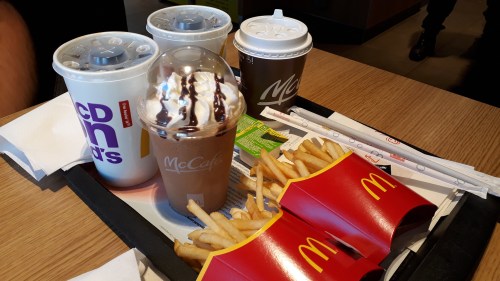 A tray with McDonald's fries, a McCafé drink topped with chocolate, and three soft drink cups.