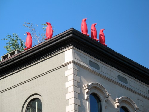 Bright red penguin sculptures perched on the roof of a building against a clear blue sky.
