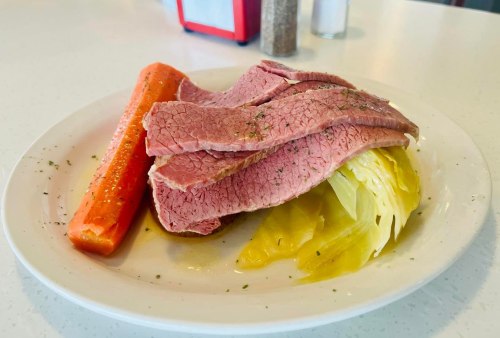 A plate of sliced corned beef with cabbage and a carrot, garnished with herbs on a white table.