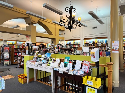 A cozy bookstore interior with shelves of books, a chandelier, and a table displaying various titles.