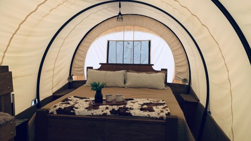 Cozy interior of a glamping tent featuring a bed, decorative throw, and two mugs on a table. Warm, inviting atmosphere.