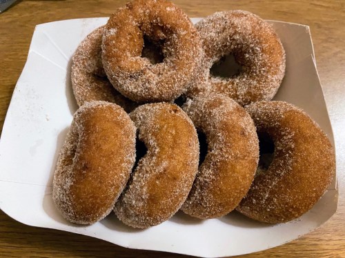A box of freshly made, cinnamon-sugar coated donuts arranged neatly.