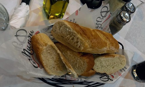 A basket of freshly baked bread rolls on a table, accompanied by olive oil and condiments.