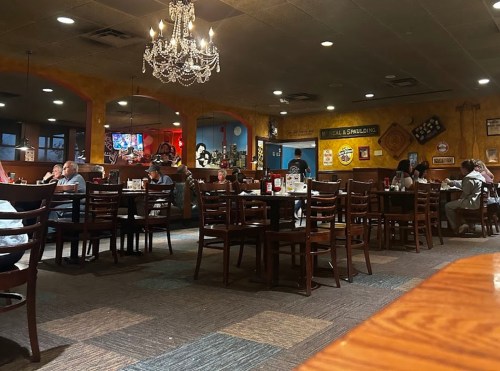 A cozy restaurant interior with wooden tables, a chandelier, and patrons enjoying their meals.