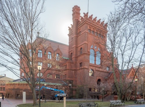 Historic red brick building with intricate architecture, surrounded by trees and a clear sky.