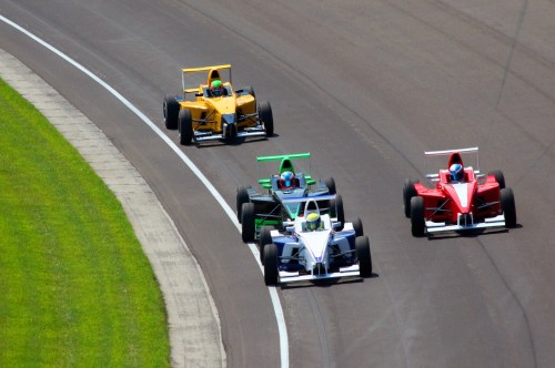 Four race cars in vibrant colors compete on a curved track, showcasing speed and excitement in a motorsport event.
