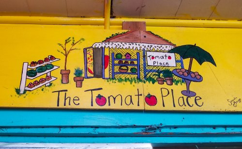 Colorful mural of "The Tomato Place" featuring a market stand, potted plants, and a sunny yellow background.