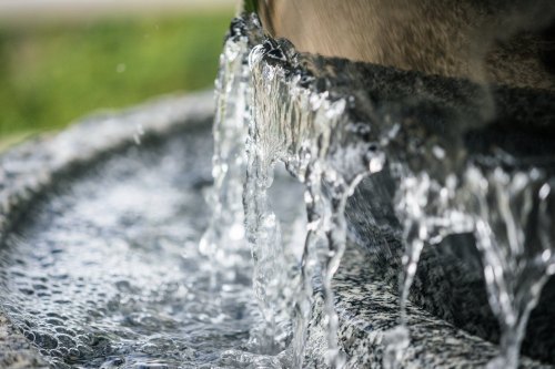 Close-up of water cascading over a stone fountain, creating ripples in a shallow pool below.