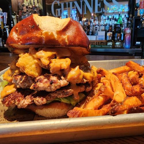 A towering burger with multiple patties, cheese, and toppings, served with a side of sweet potato fries.