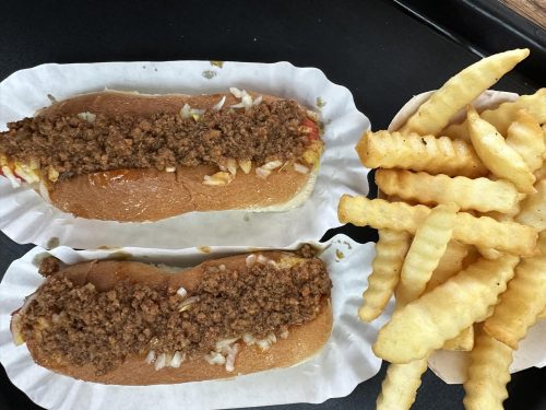Two hot dogs topped with chili and onions, served with a side of crinkle-cut fries.