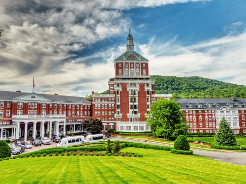 Historic hotel building with a clock tower, surrounded by lush greenery and a blue sky with clouds.