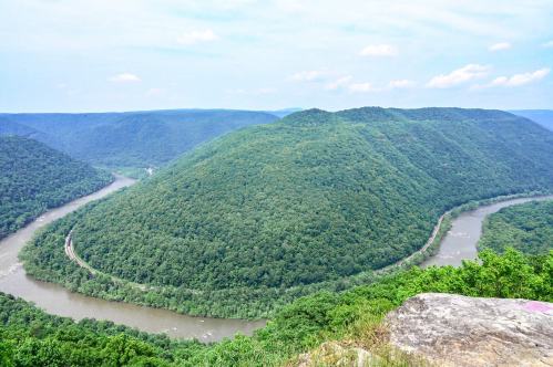 A scenic view of a winding river surrounded by lush green hills under a blue sky.