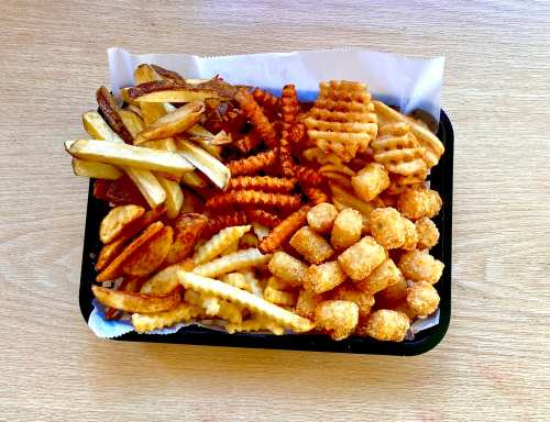 A tray filled with various types of fries, including crinkle-cut, curly, and tater tots, on a wooden surface.