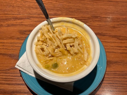 A bowl of creamy soup topped with crispy tortilla strips, placed on a blue plate with a napkin underneath.