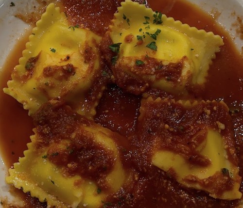 Four ravioli in a rich tomato sauce, garnished with herbs, served in a white bowl.