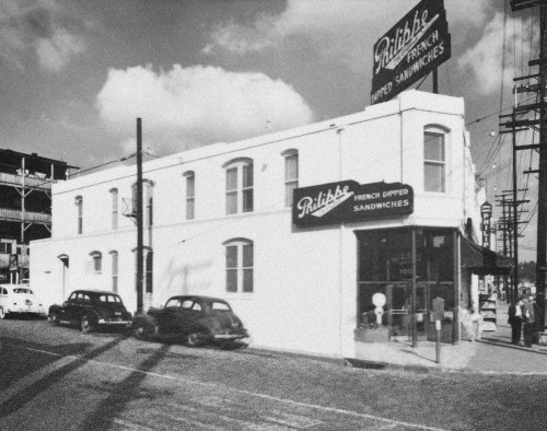Historic black-and-white photo of a sandwich shop with a sign reading "Philippe French Dipped Sandwiches" and vintage cars parked outside.