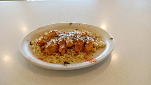 A plate of chicken in a creamy sauce served over a bed of rice, garnished with spices on a white table.