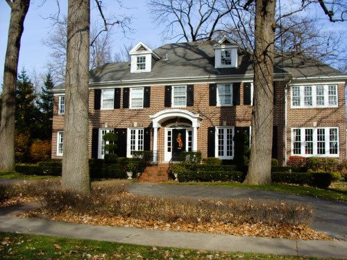 A large brick house with a gray roof, surrounded by trees and autumn leaves, featuring a welcoming front porch.