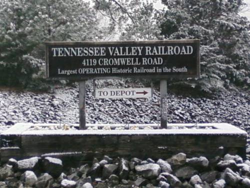 Sign for Tennessee Valley Railroad, indicating direction to depot, surrounded by snow-covered ground and trees.