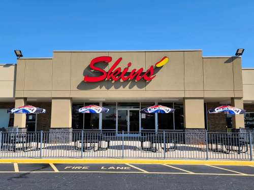 Exterior of Skins restaurant with colorful umbrellas on the patio and a clear blue sky above.