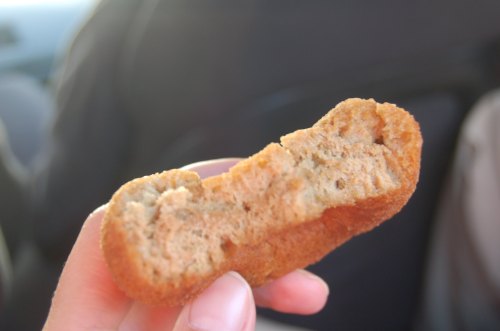 A hand holding a partially bitten chicken nugget, revealing its textured interior.