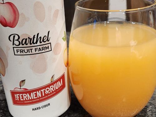 A glass of cloudy hard cider next to a bottle labeled "Barthel Fruit Farm" from "The Fermentorium."